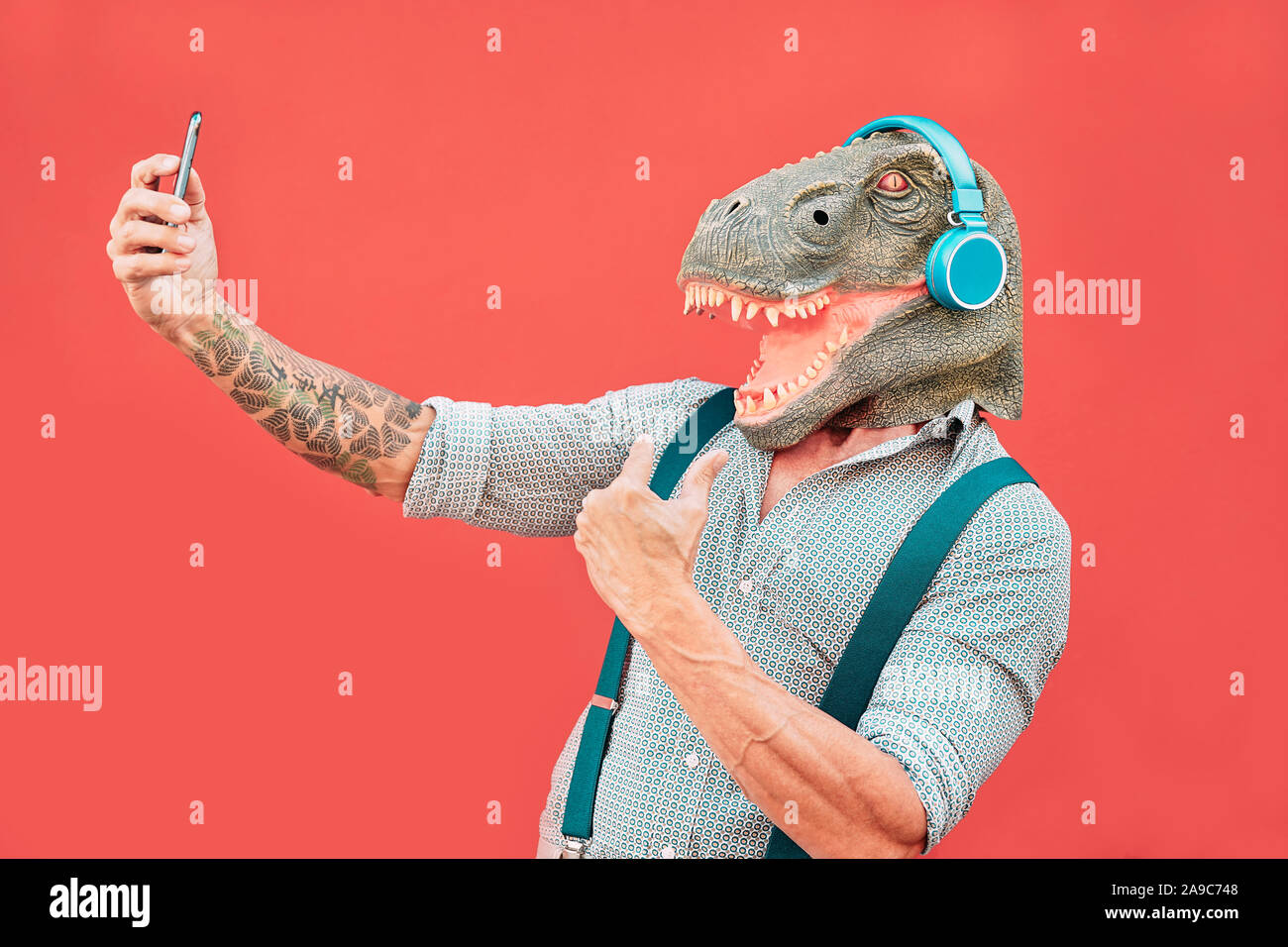 Crazy man wearing t-rex masque et en tenant avec selfies mobile smartphone - Hipster masculins plus âgés ayant du plaisir à l'écoute de la musique et de la danse piscine Banque D'Images