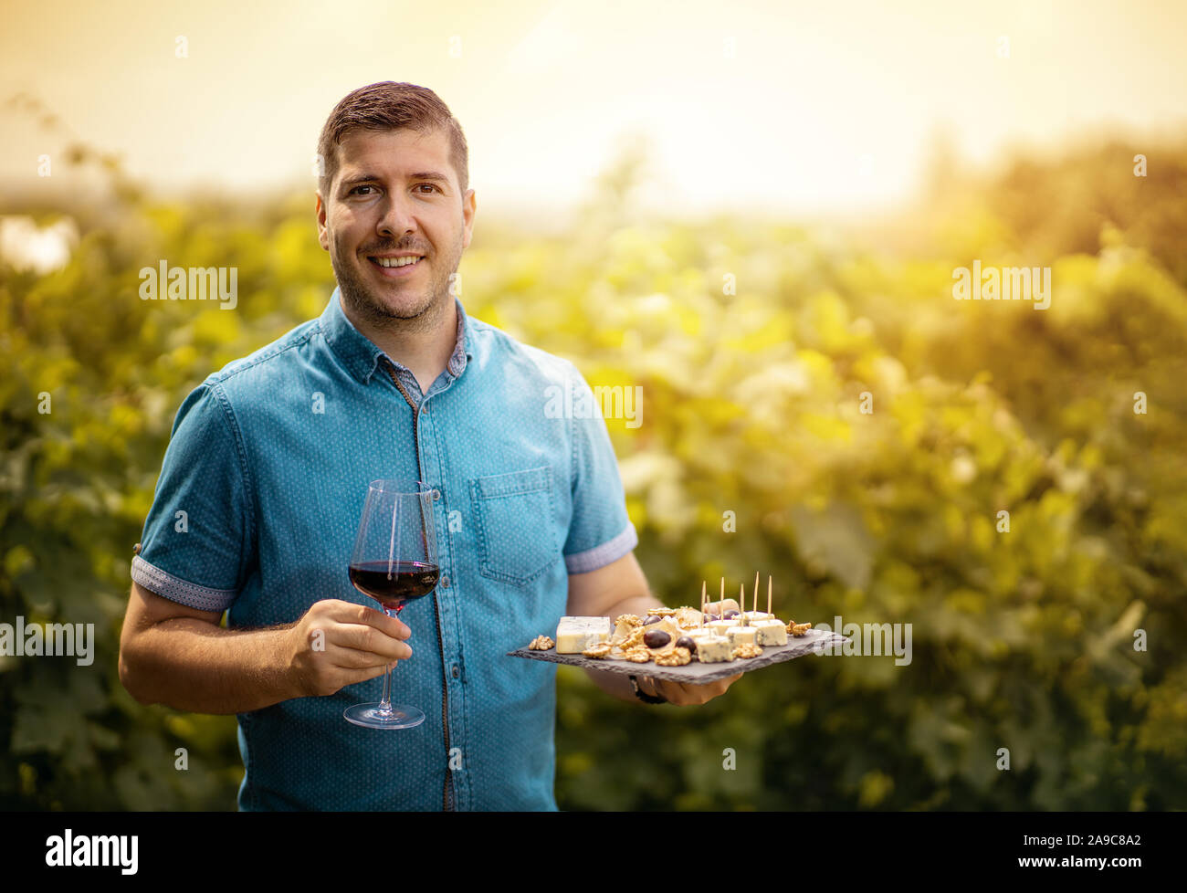 Verre de vin rouge dans la main d'un jeune vigneron dans le Vignoble - Dégustation de vin - visite touristique accueillant l'homme au coucher du soleil dans la cave. Tonique Banque D'Images