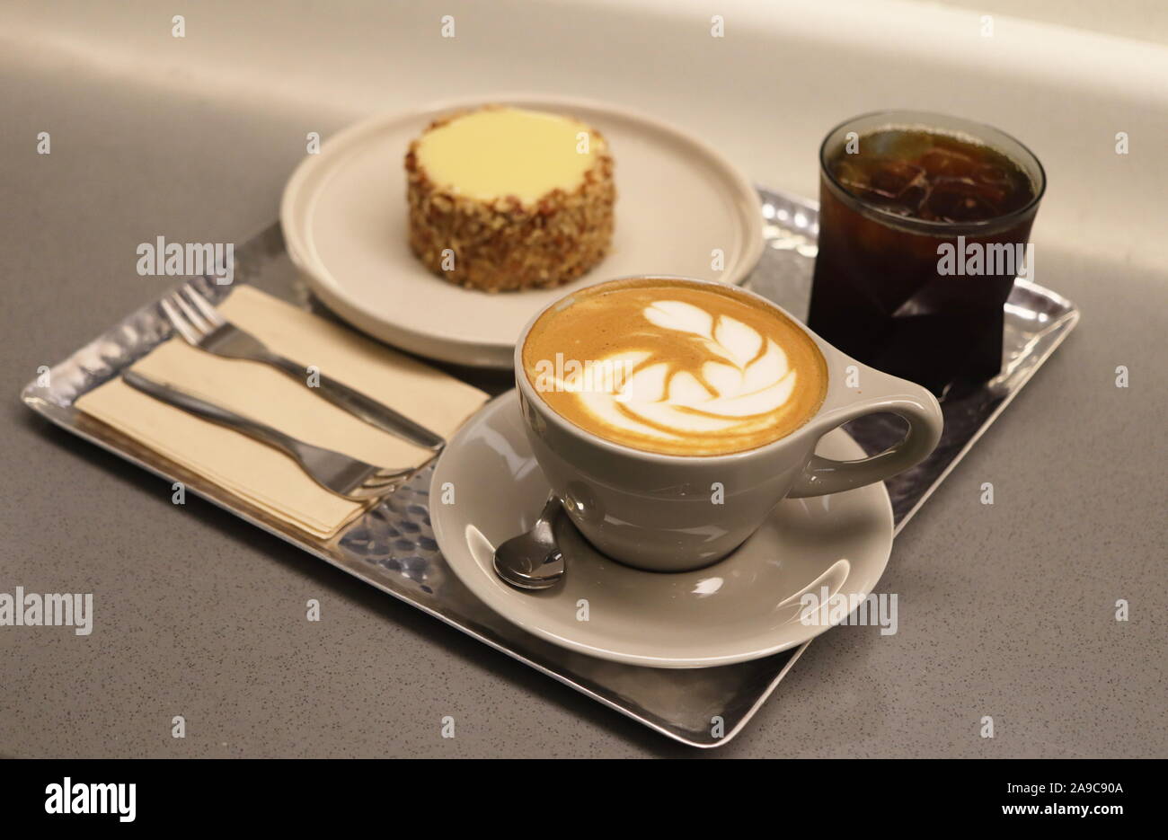 Plateau avec tasse de café décoré de feuille, gâteau, fourches, et du café noir dans un verre contre un arrière-plan gris Banque D'Images