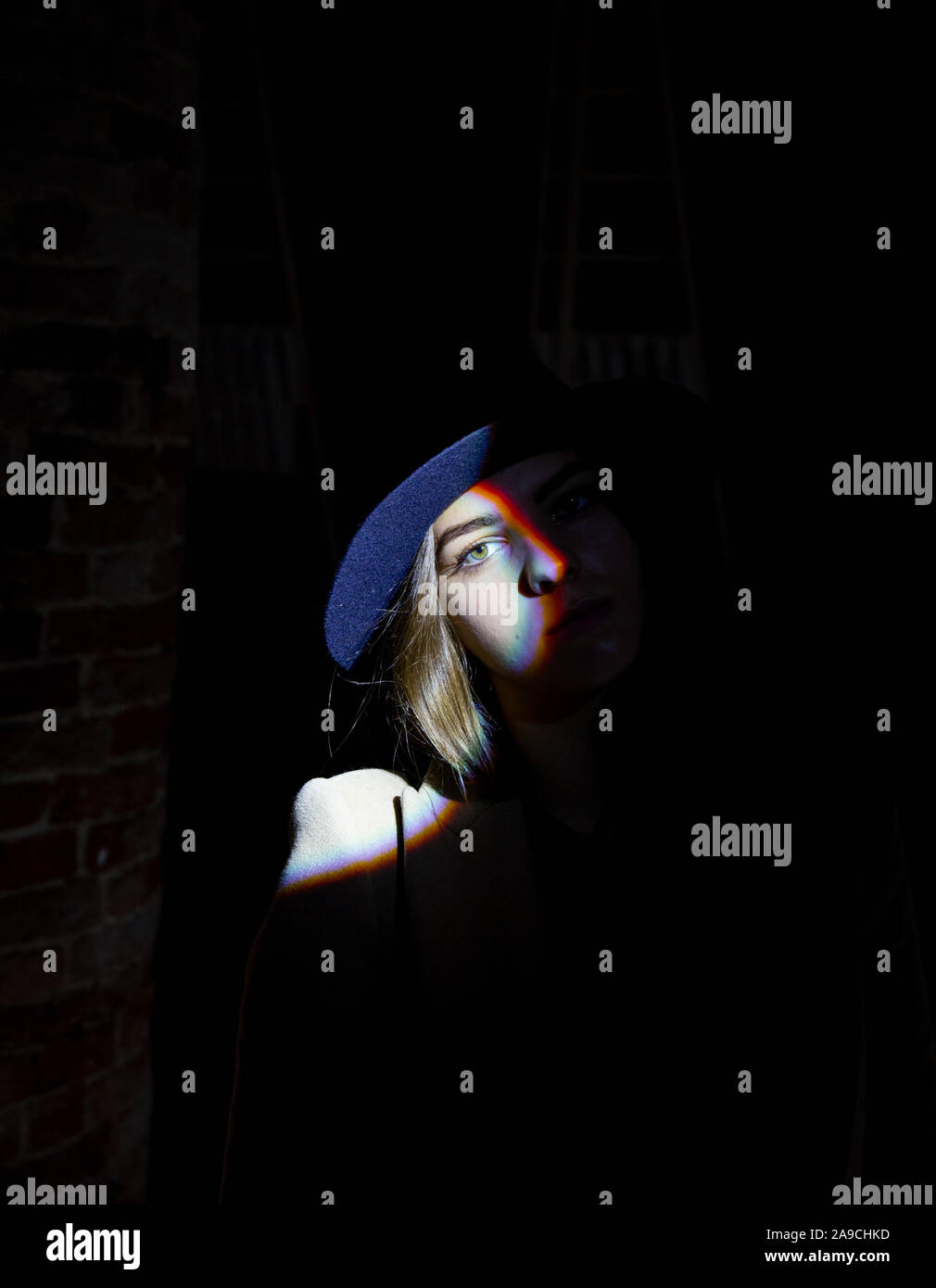 Mystérieuse Jeune fille avec chapeau avec une lumière sombre contraste sur Arc-en-ciel des yeux Visage Banque D'Images