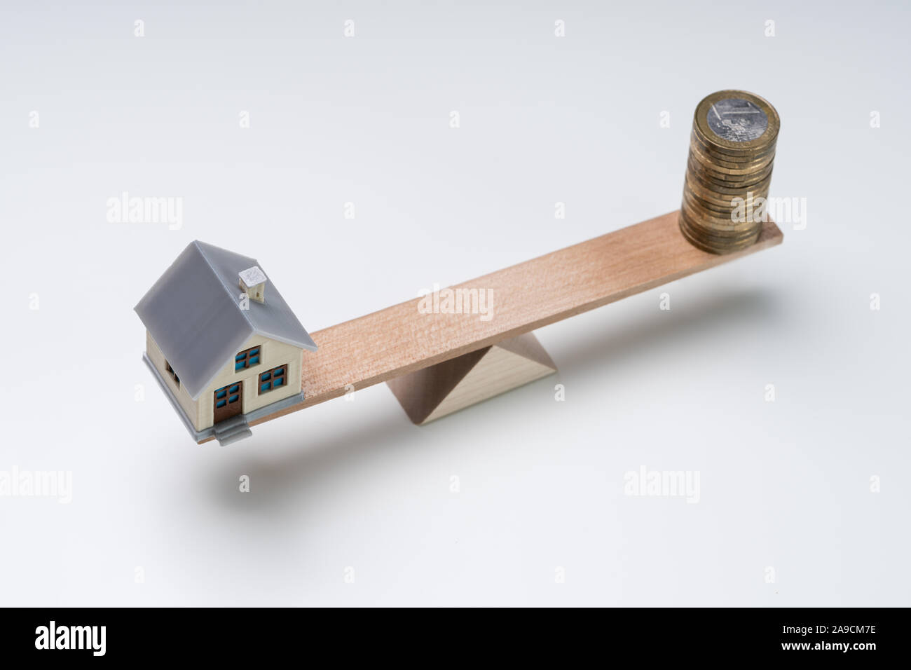 De pièces empilées et Miniature House On Wooden Seesaw Against White Background Banque D'Images