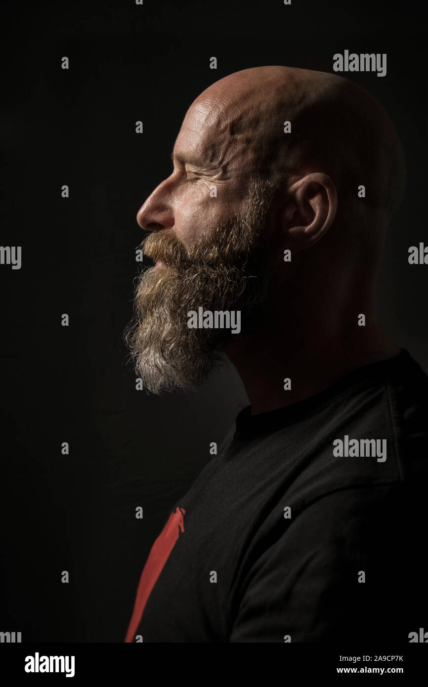 Une image d'un homme barbu aux yeux clos Vue de côté et un arrière-plan sombre Banque D'Images