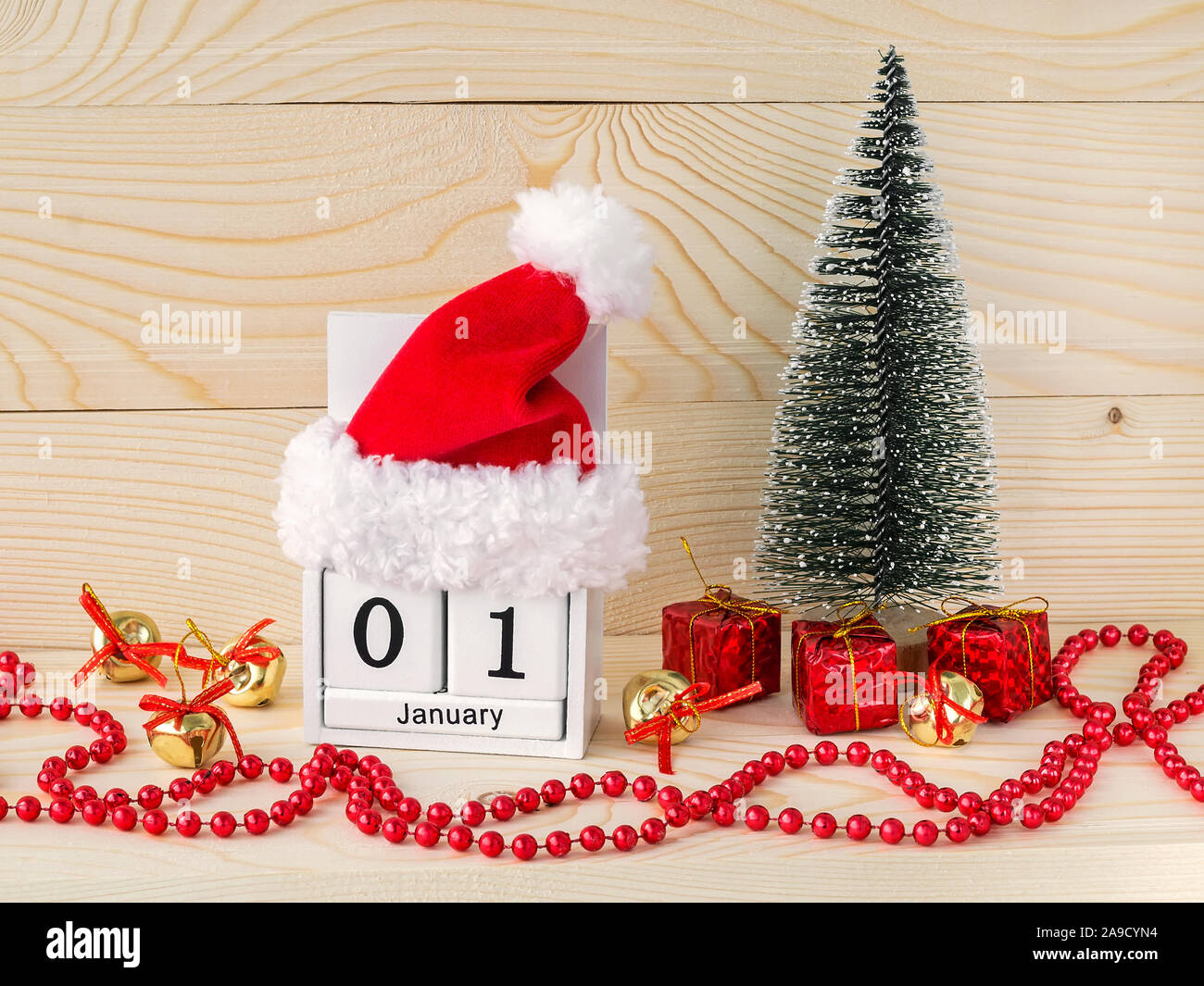 Santa Claus hat rouge sur un calendrier perpétuel en bois blanc avec date 01 janvier. Arbre de Noël et guirlande perle rouge sur un fond de bois naturel. Banque D'Images