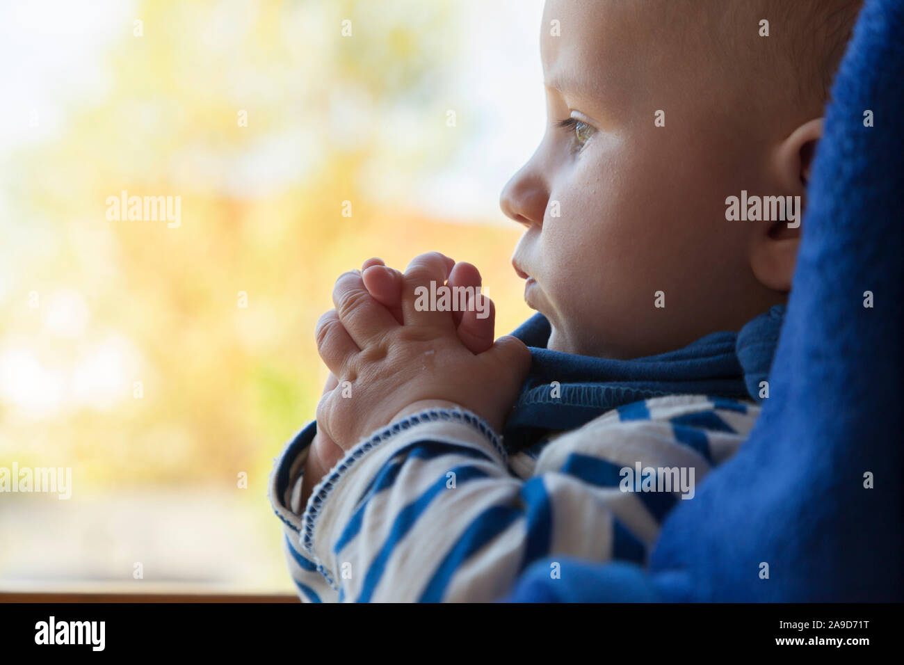 Bébé assis dans une chaise haute, les mains devant la bouche, tête, portrait, sur les côtés, en arrière-plan lumineux Banque D'Images