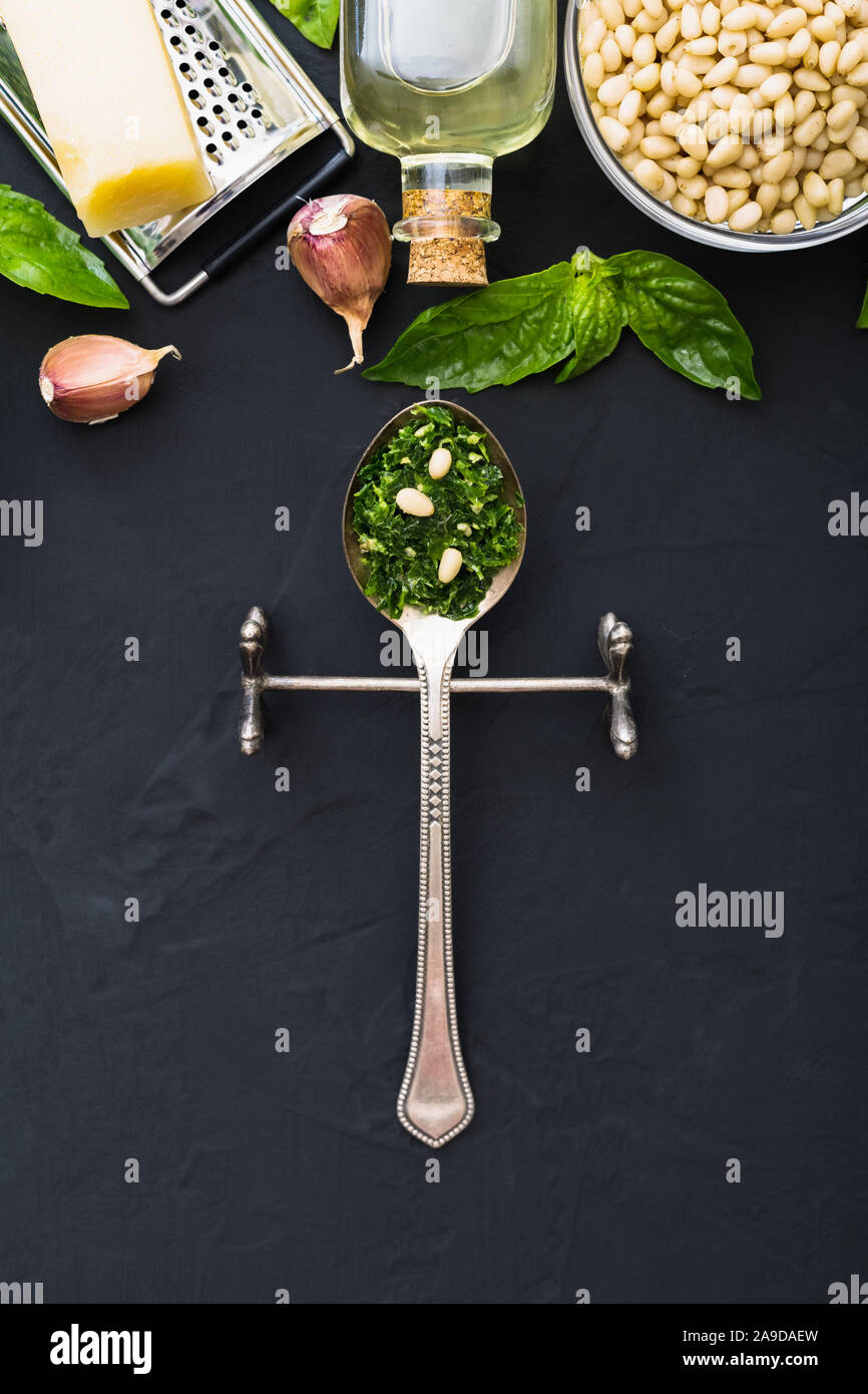Sauce Pesto dans une cuillère vintage avec des ingrédients : les pignons de pin, basilic vert, l'ail, parmesan, huile d'olive sur fond de ciment noir foncé. Recette italienne Banque D'Images