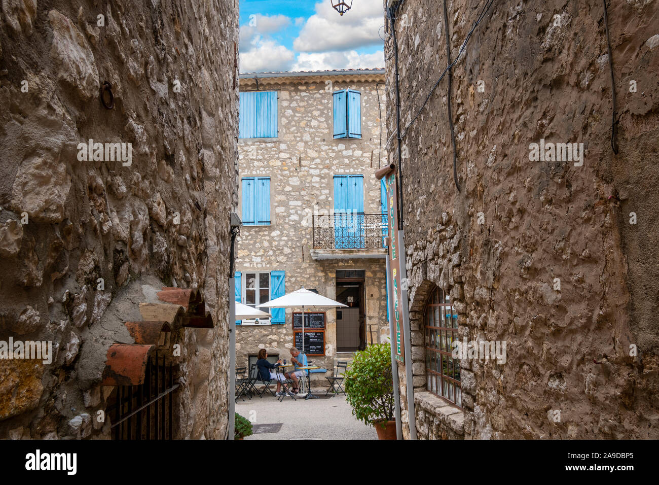 Un couple mange à midi sur la terrasse d'un café avec terrasse sous les volets bleus français dans le village médiéval historique de Gourdon France Banque D'Images