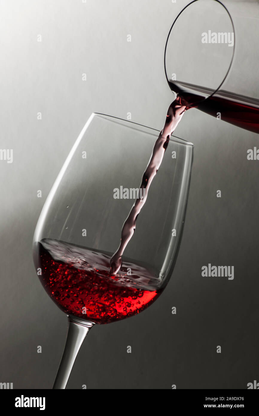Studio shot of red wine le remplissage d'un verre dans un autre en face de fond texturé doux avec gradient de lumière-obscurité. Banque D'Images