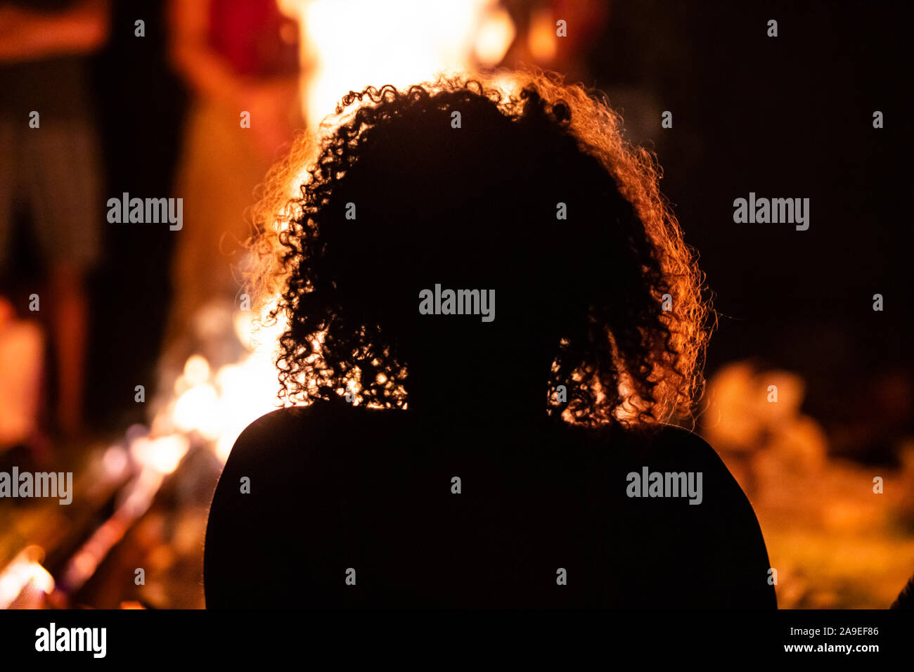 Silhouette d'un cheveux boucles femme assise à l'avant de l'incendie, vu de dos au cours de la nuit noire de camp, arrière-plan flou Banque D'Images