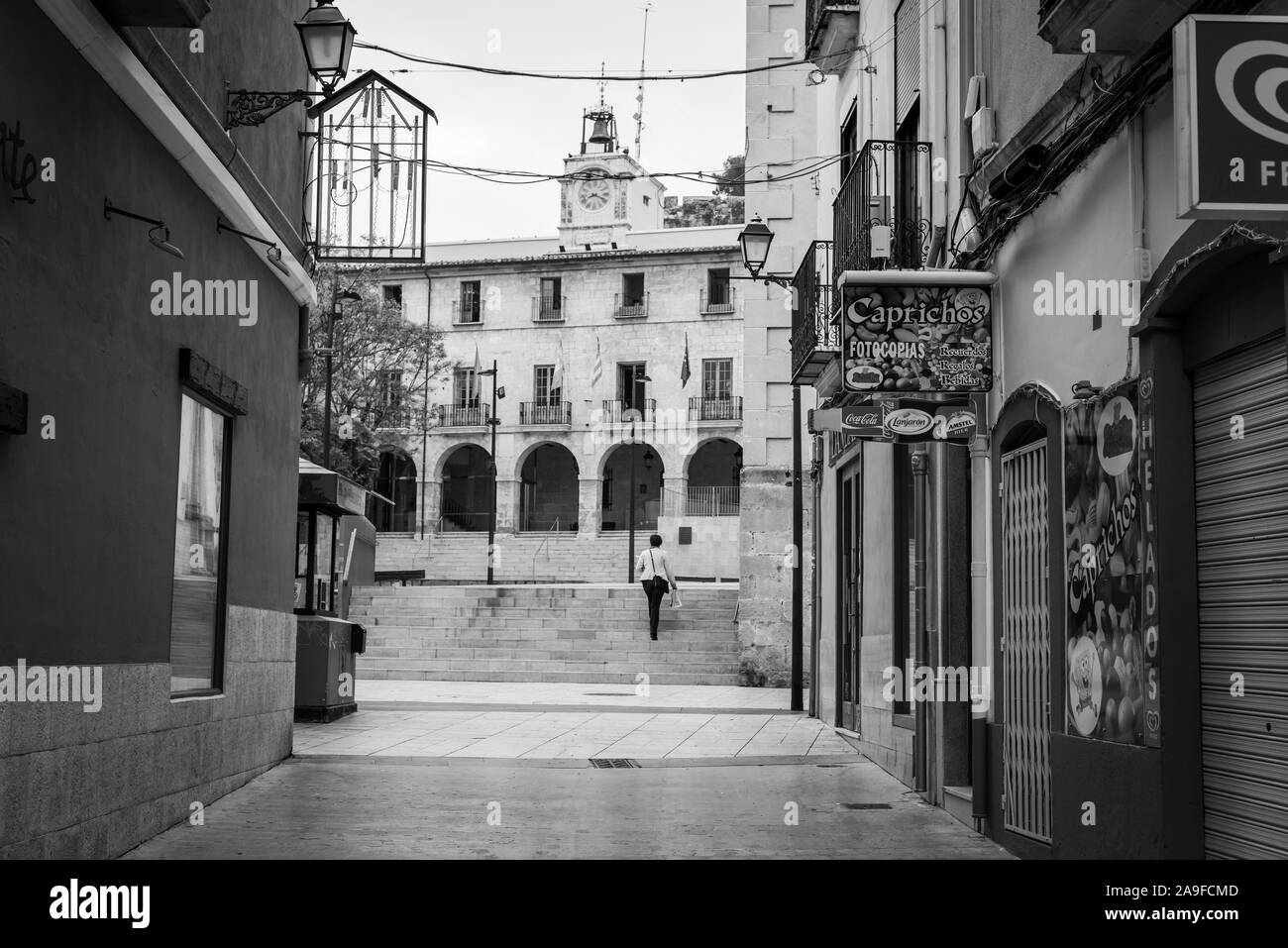 Une femme se présente comme suit en direction de l'hôtel de ville et des ateliers fermés tôt le matin dans la région de Denia, Espagne. Banque D'Images