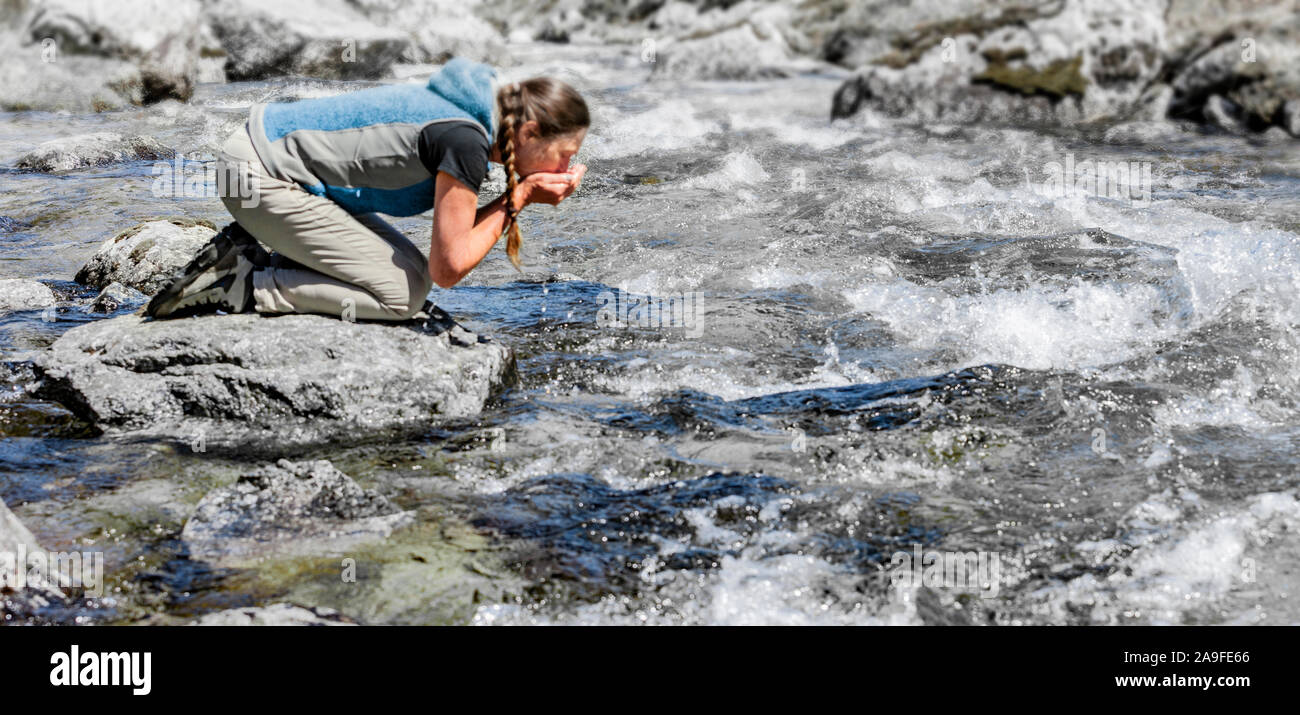 Femme buvant de l'eau d'un ruisseau de montagne Banque D'Images