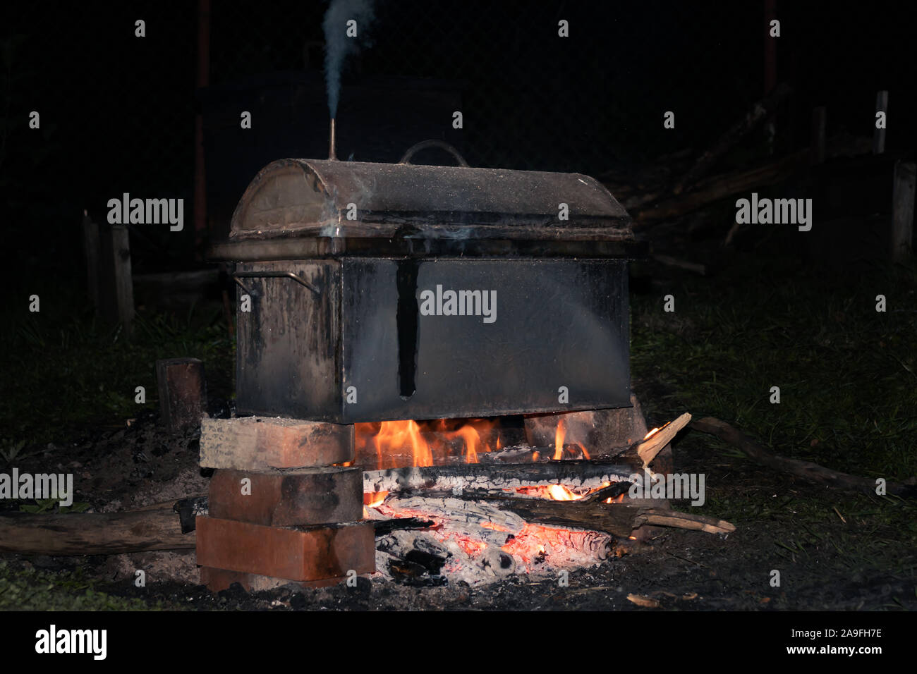 La cuisson des viandes fumées dans un fumoir métalliques mobiles sur le bûcher Banque D'Images