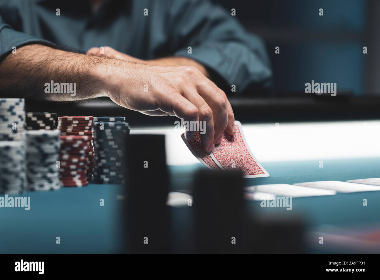 Tournoi caritatif de poker Texas Hold'em au casino, un joueur tient deux cartes, des piles de jetons sur la table Banque D'Images