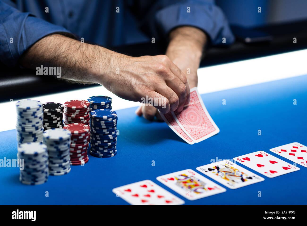Tournoi caritatif de poker Texas Hold'em au casino, un joueur tient deux cartes, des piles de jetons sur la table Banque D'Images