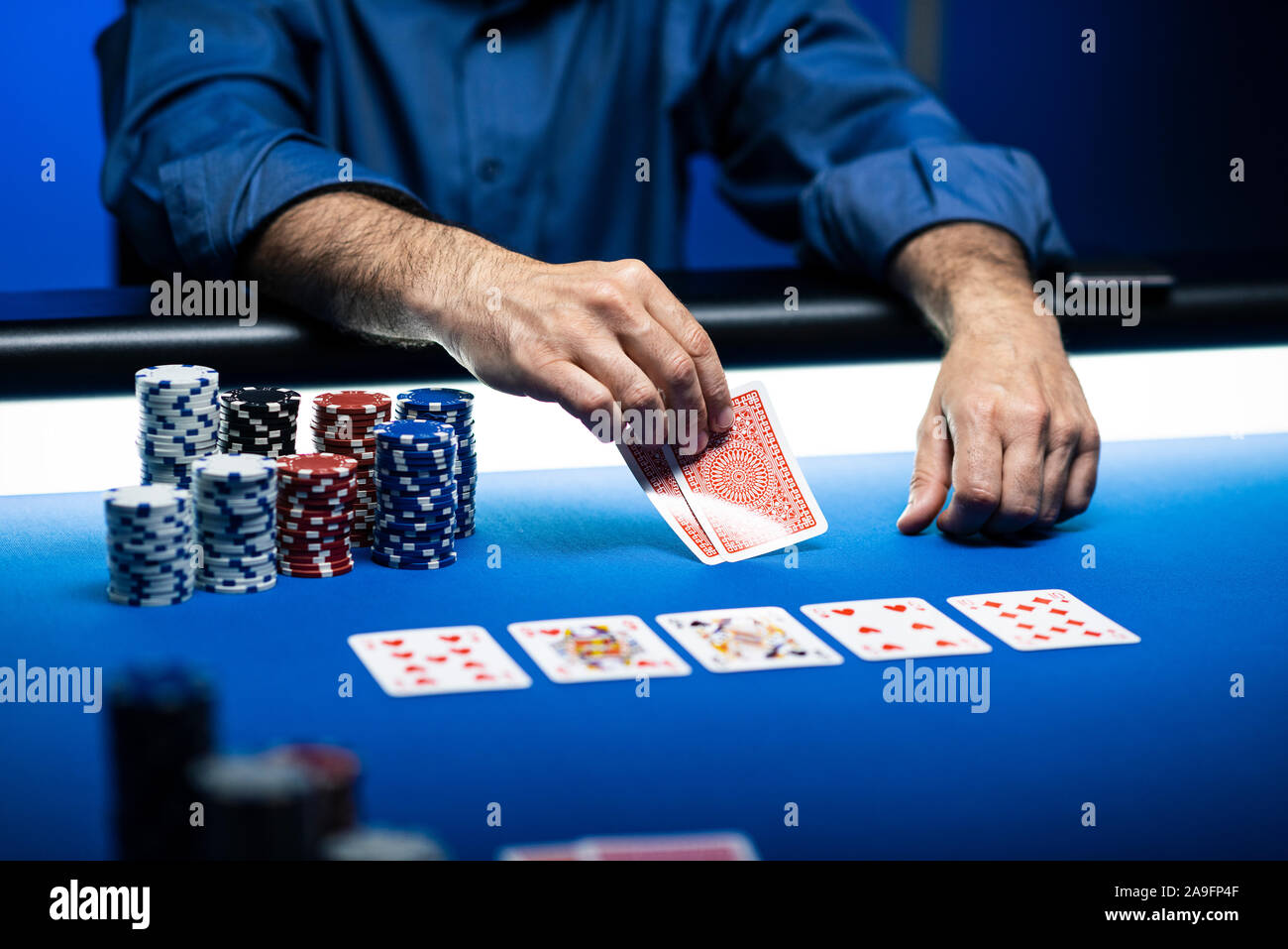 Tournoi caritatif de poker Texas Hold'em au casino, un joueur tient deux cartes, des piles de jetons sur la table Banque D'Images
