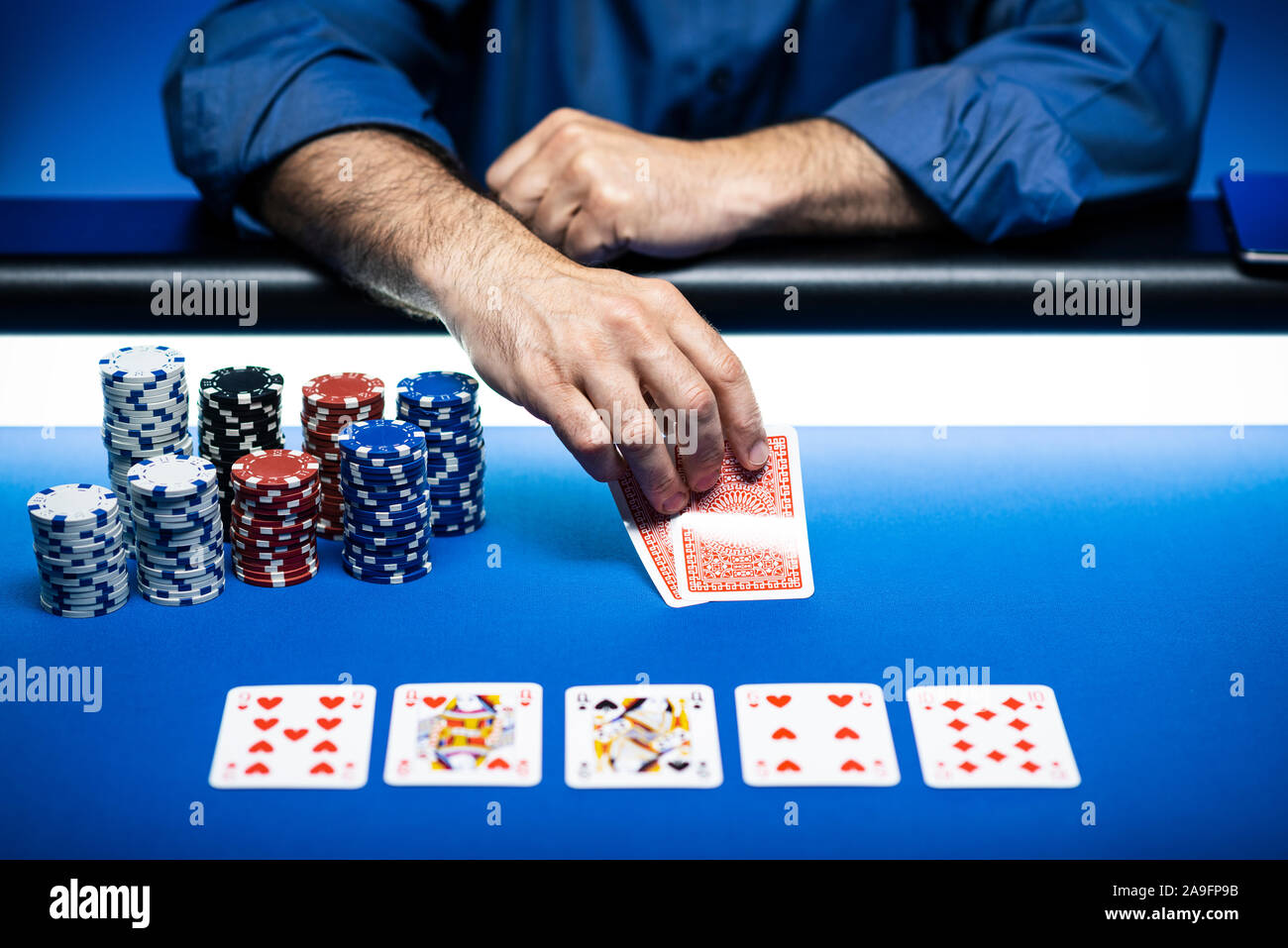 Tournoi caritatif de poker Texas Hold'em au casino, un joueur tient deux cartes, des piles de jetons sur la table Banque D'Images