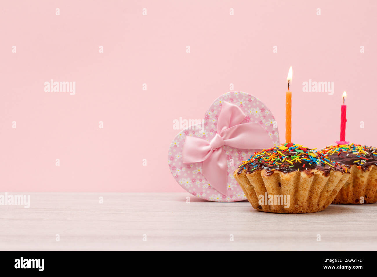 Boîte-cadeau en forme de cœur et de délicieux muffins anniversaire avec lustre de chocolat et caramel, décorée avec des bougies pour fêtes de gravure sur bois et bac rose Banque D'Images