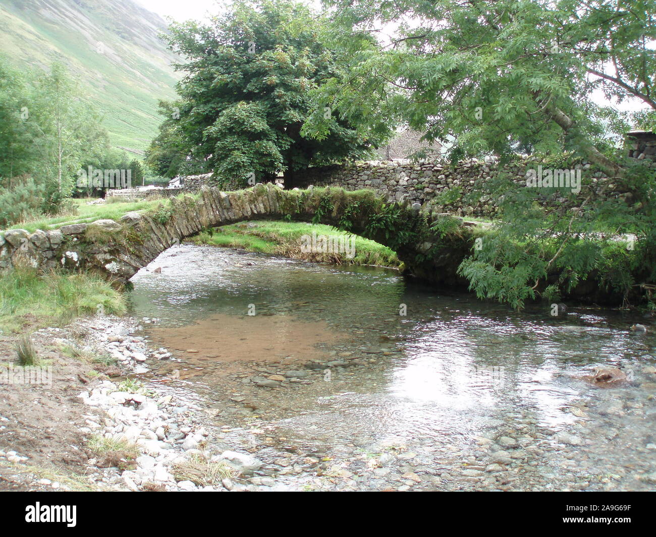 Montrant un paysage d'eau claire dans les collines du parc national de lake district qui a une passerelle construite en pierre voûtée traverser le ruisseau. Banque D'Images