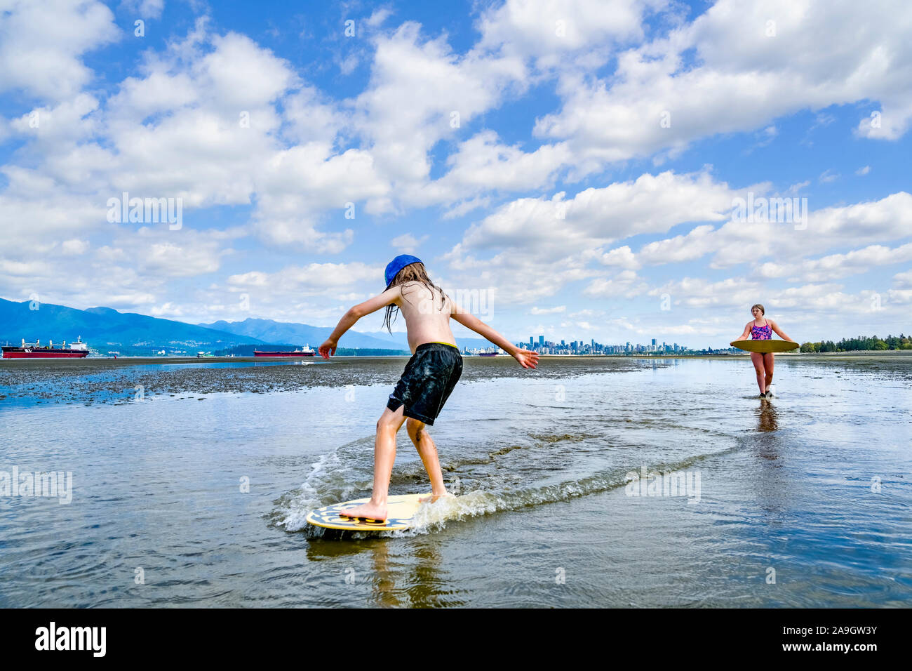 Jeune garçon aux cheveux longs, skimboarding banques espagnoles, English Bay, Vancouver, British Columbia, Canada Banque D'Images