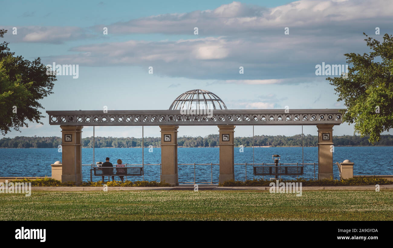 Un couple est assis sur un banc dans un parc sur le lac Monroe au centre-ville de Sanford, Floride. Banque D'Images