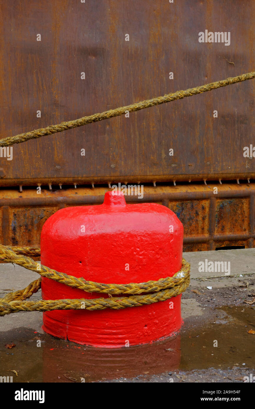 Corde d'un navire attaché à un vieux bollard d'amarrage en béton rouge sur un quai. Banque D'Images