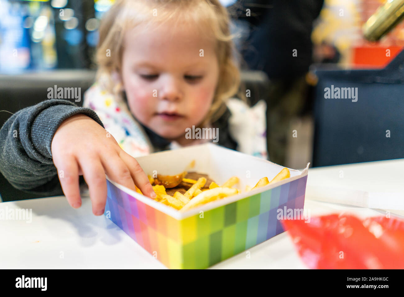 Une jolie petite fille mange son happy meal à partir de la zone prévue,  frites et hamburgers pour un festin qui vient avec un ours en peluche avec  TY-d'yeux Photo Stock -