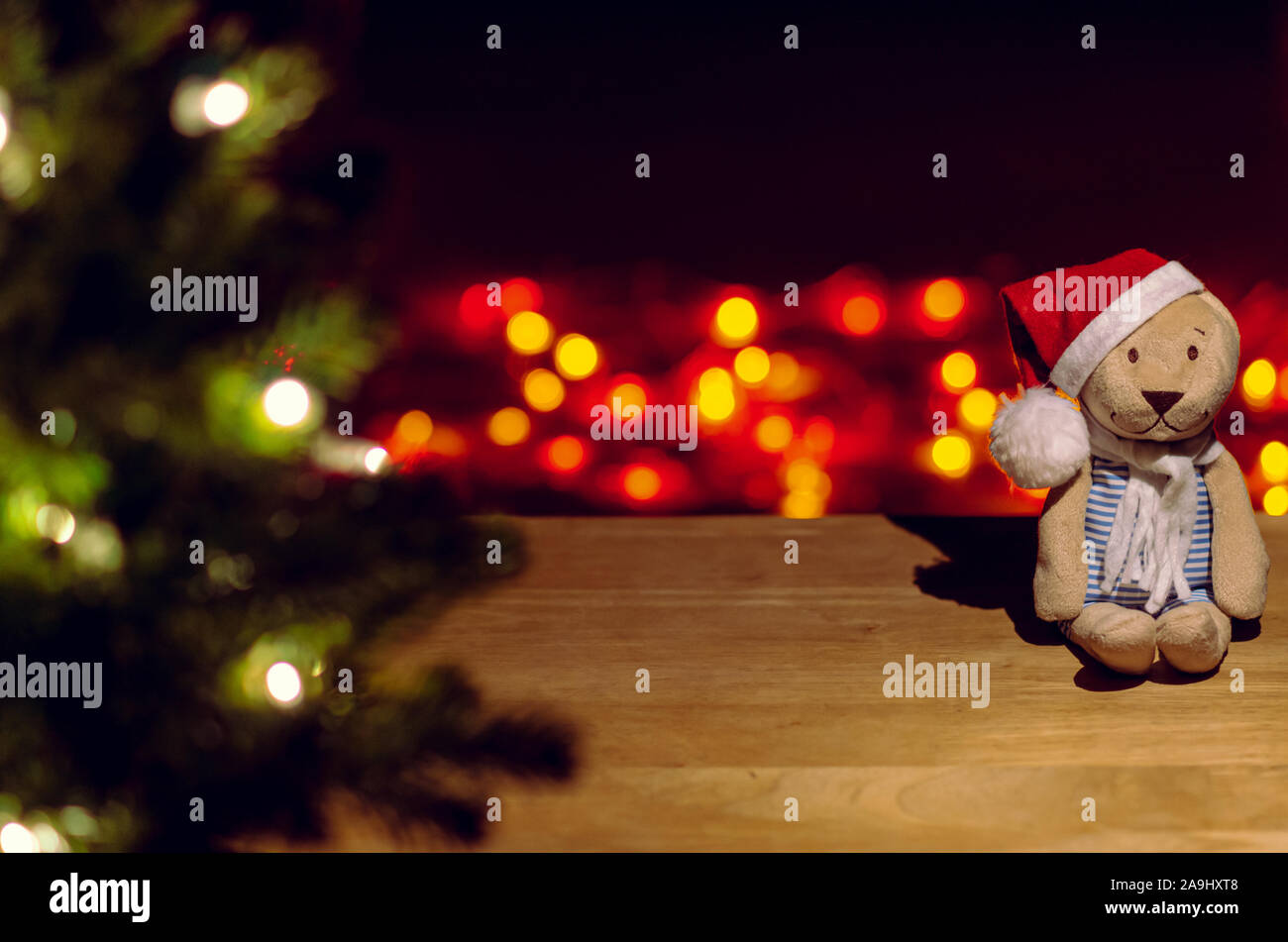 Père Noël ours assis sur table en bois avec arbre de Noël coloré et lumières fond flou. Banque D'Images