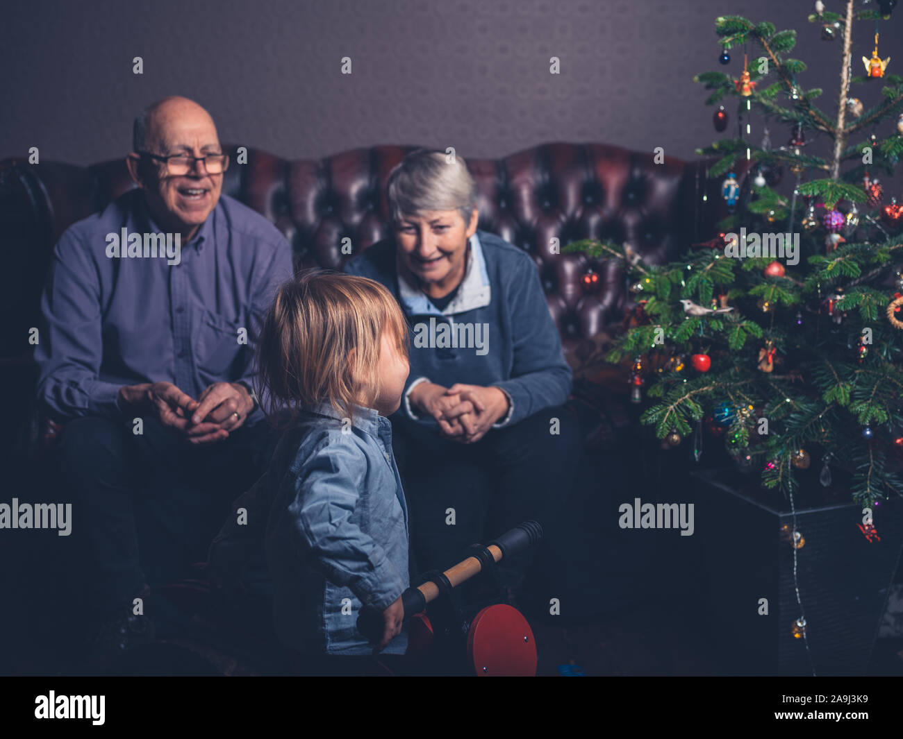 Un petit enfant et ses grands-parents sont assis sur un canapé près de l'arbre de Noël Banque D'Images