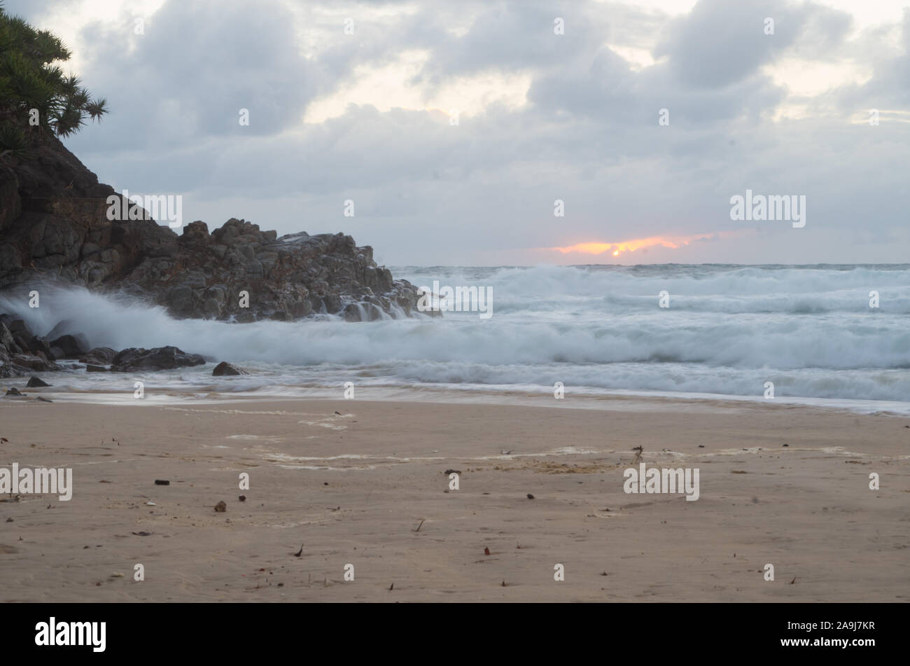 Lever de soleil sur l'horizon à une plage par une pointe avec des vagues se briser Banque D'Images