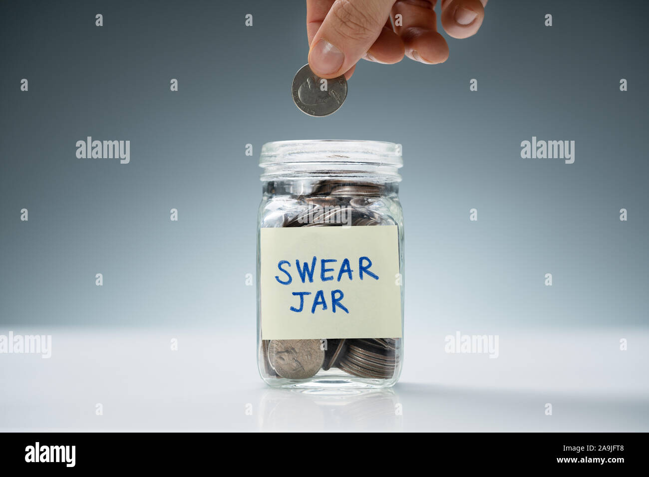 Sa main l'insertion d'une pièce de monnaie pour jurer avec bol en verre blanc plus de texte Jar 24 Banque D'Images