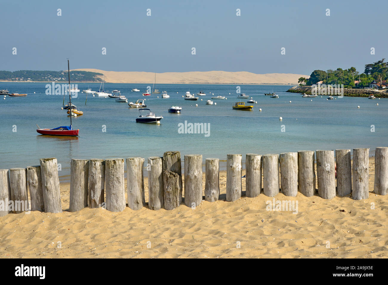 Plage avec des troncs de bois protégeant les dunes de Cap-Ferret, bateaux et la dune du Pilat dans l'arrière-plan. Située dans le département de la Gironde France Banque D'Images