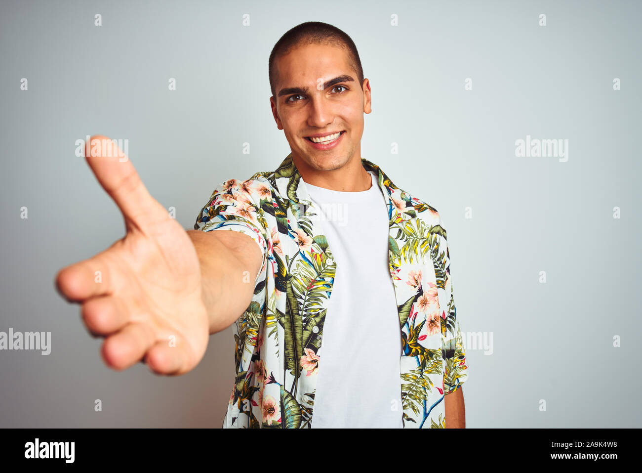 Jeune homme séduisant en vacances portant chemise hawaïenne sur fond blanc smiling friendly offrant comme message d'handshake et accueillant. Succès Banque D'Images