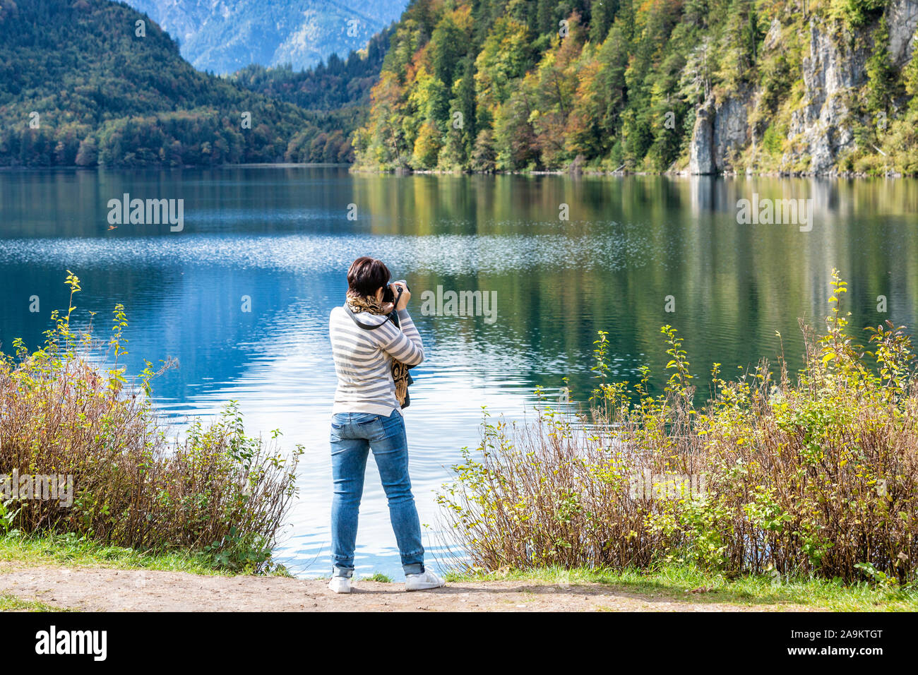 Une femme se tient sur la rive du lac Schwansee en Allemagne et prend des photos de beaux paysages d'automne. Banque D'Images