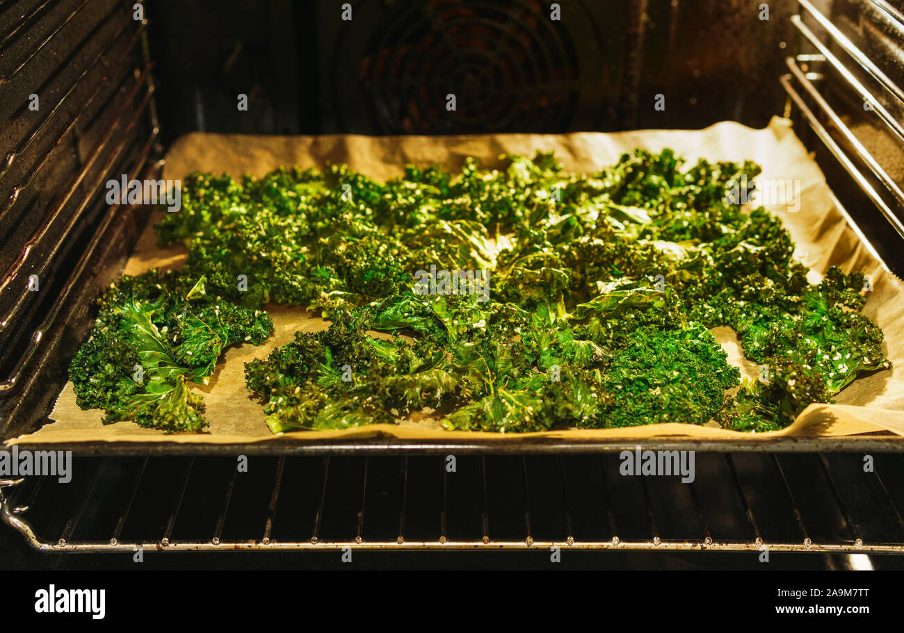 Kale chips croustillante fraîchement préparés sur une plaque à pâtisserie papier cuisson dans un four allumé à ouvrir la porte du four - vue oblique, format paysage horizontal Banque D'Images