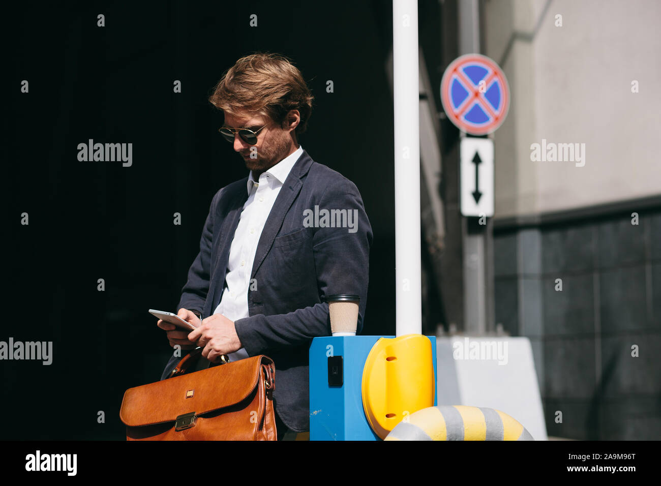 Un homme en costume est debout dans un Parking La lecture des nouvelles sur un téléphone mobile Banque D'Images