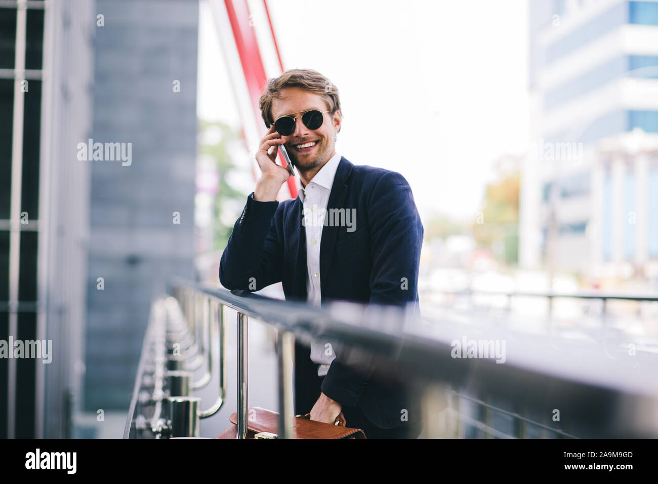 Manager en lunettes sourit tout en parlant sur un téléphone cellulaire dans la rue Banque D'Images