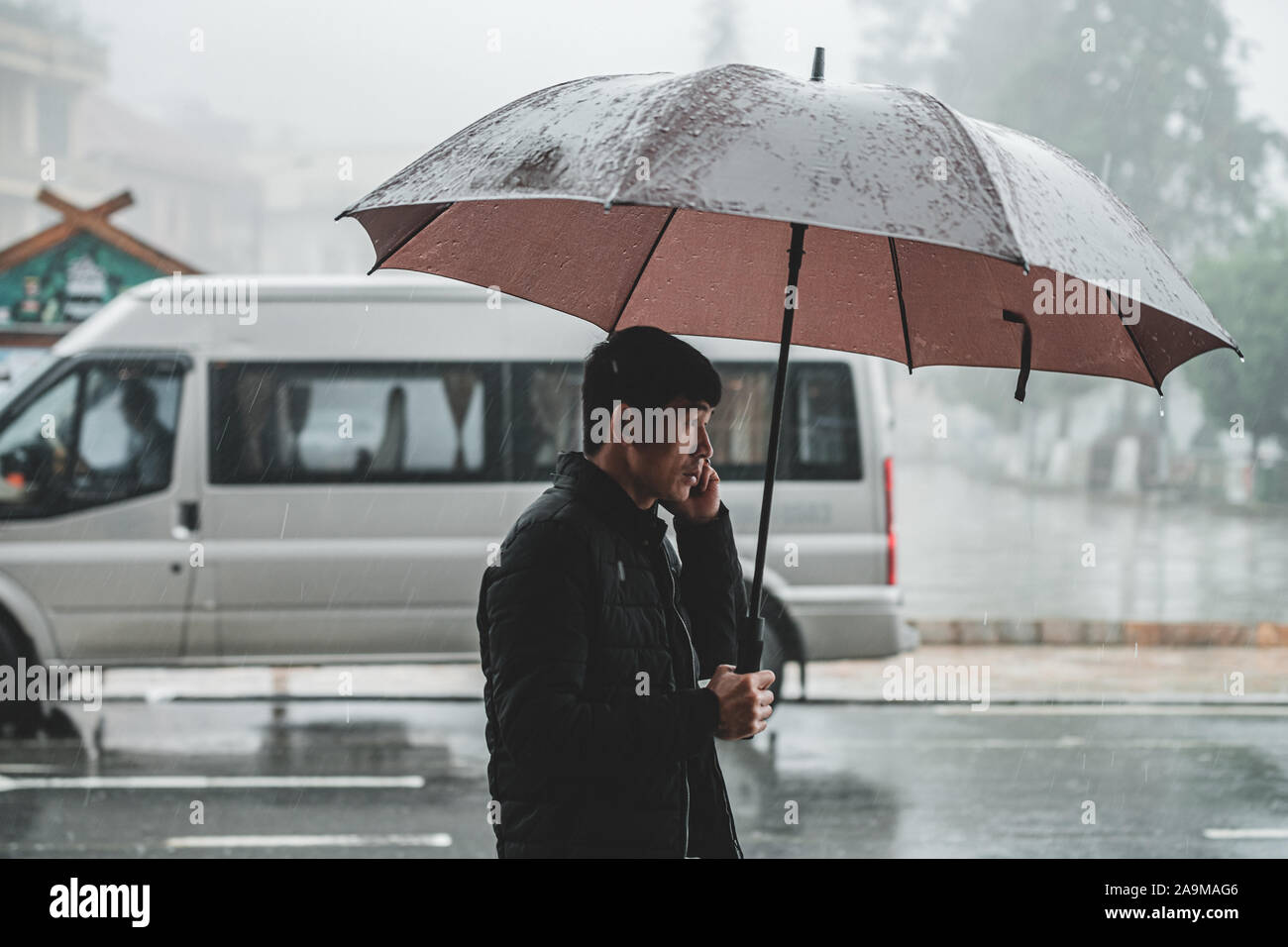 Sapa, Vietnam - 13 octobre 2019 : Un homme asiatique d'âge moyen passe devant l'appareil photo sous la pluie sous un parapluie dans la petite ville de montagne de Sapa Banque D'Images
