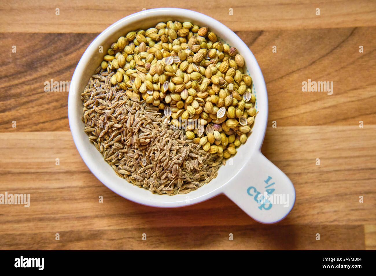 Quart de tasse mesurer contenant un mélange de cumin et coriandre Graines épices vu de dessus sur une surface de travail en bois Banque D'Images