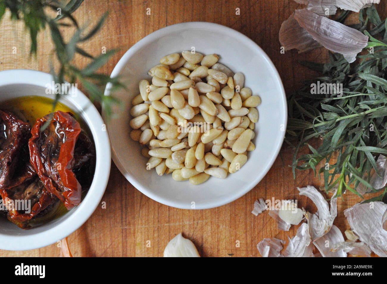 Les noix de pin, l'estragon et les tomates séchées dans des bols en céramique blanche Banque D'Images