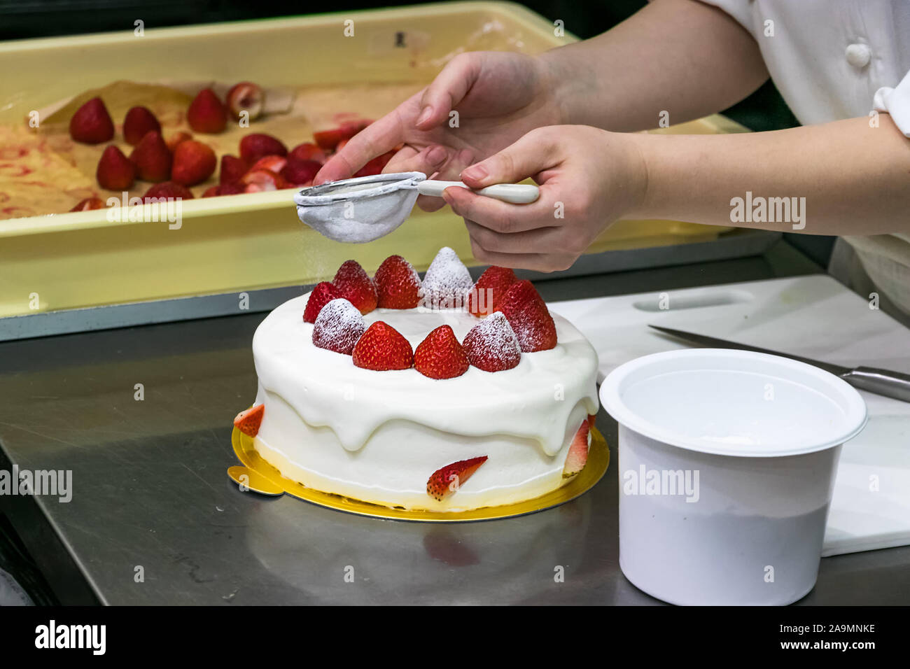 Chef pâtissier femelle mains, Décorer un gâteau aux fraises avec du sucre en poudre Banque D'Images