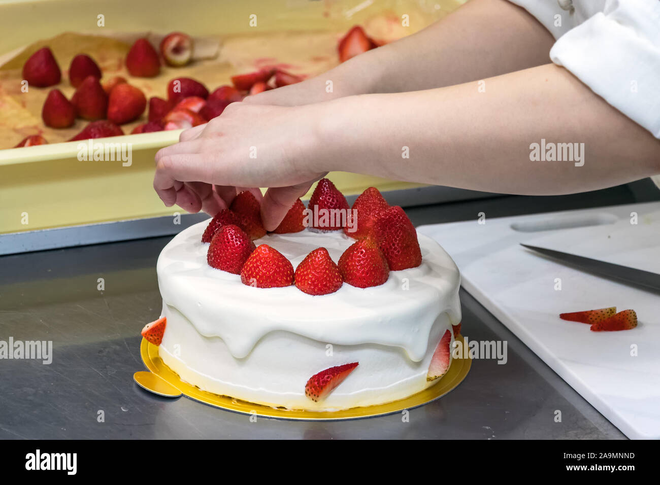 Chef pâtissier femelle mains, Décorer un gâteau à la crème avec les fraises. Banque D'Images