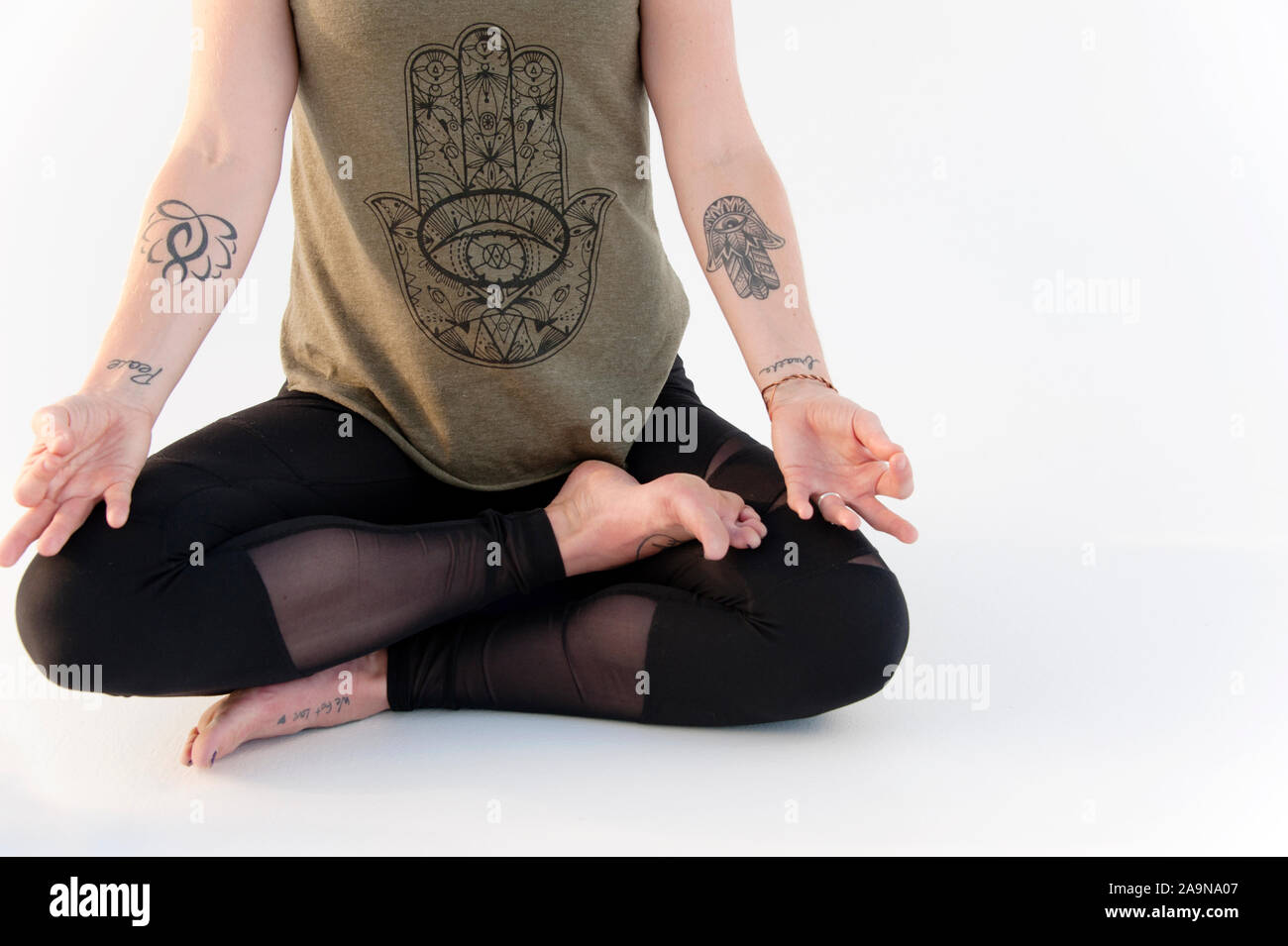 Au niveau des épaules recadrée woman practicing yoga asana sur un fond blanc. Elle porte un tee shirt et Main Hamsa yoga a des tatouages. Banque D'Images