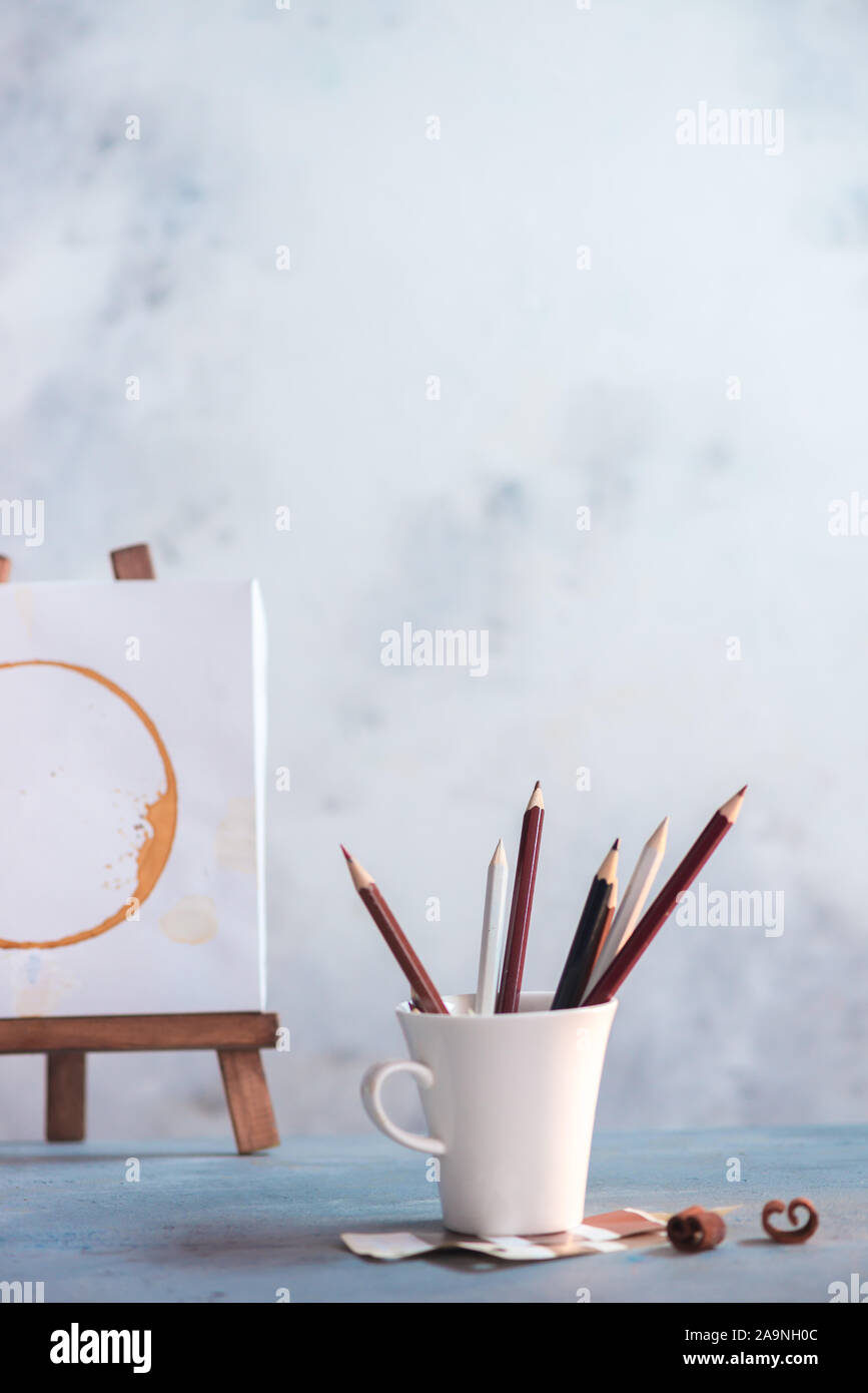 Travail de l'artiste avec des tasses à café, des crayons, des échantillons et un chevalet en bois sur un fond clair avec Banque D'Images