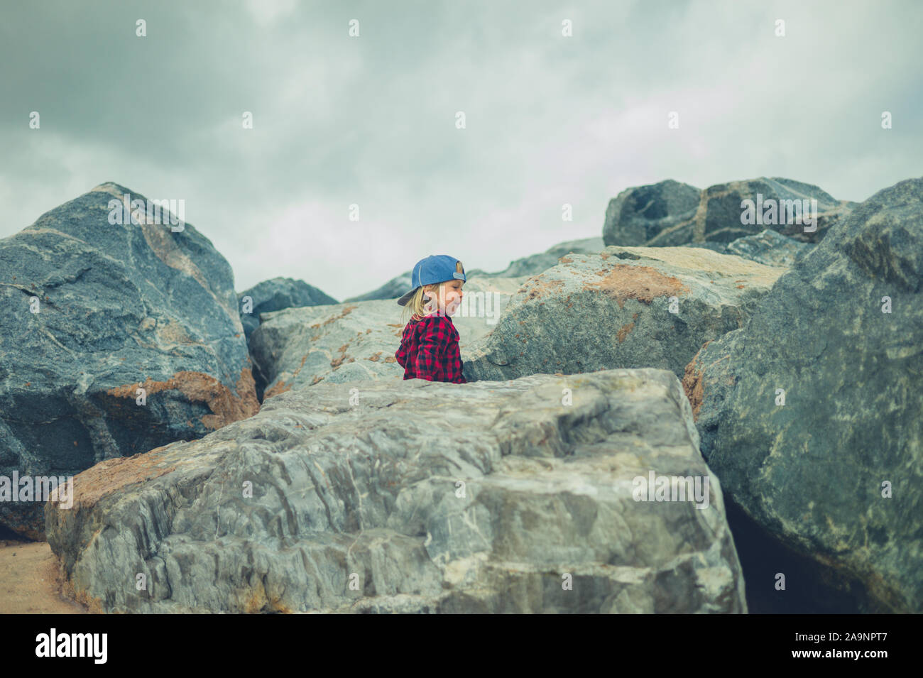 Un petit enfant est l'escalade sur quelques roches sur une journée d'été nuageux Banque D'Images
