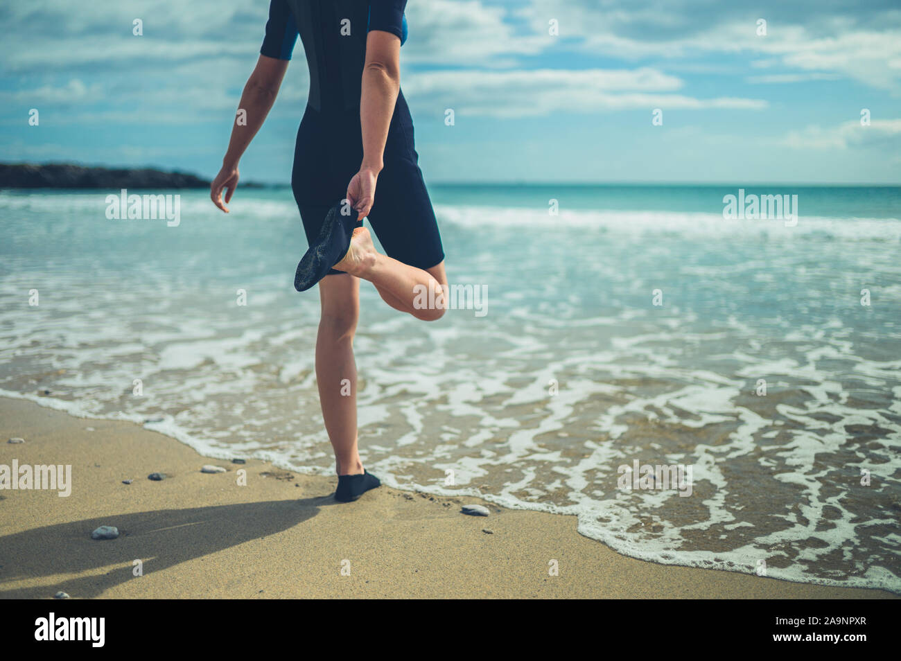 Une jeune femme dans une combinaison de plongée sur la plage met ses  chaussures imperméables Photo Stock - Alamy