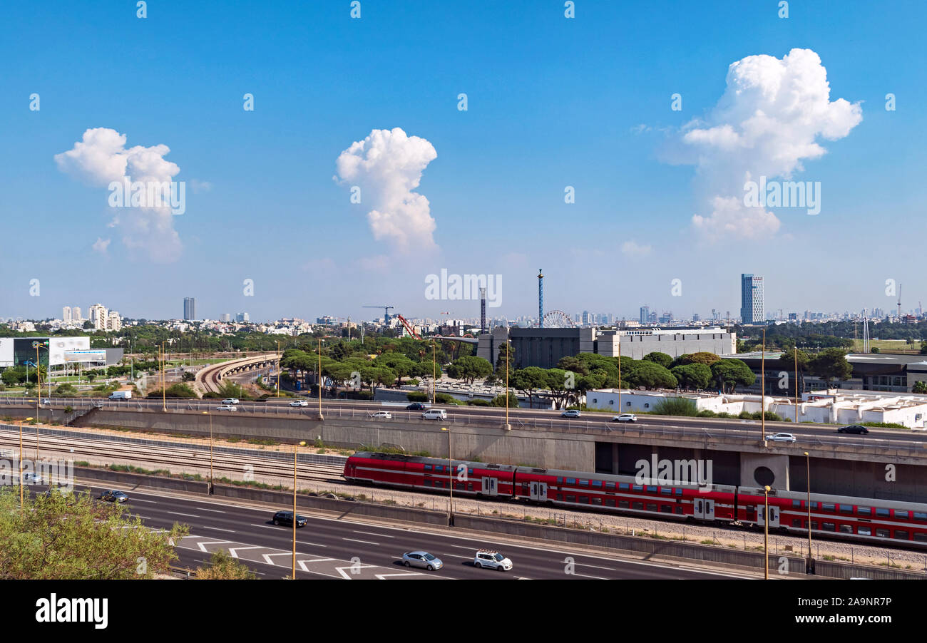 Trois nuages au-dessus de la thunder nord de Tel aviv skyline avec luna park, l'autoroute ayalon, et un train à l'avant-plan Banque D'Images