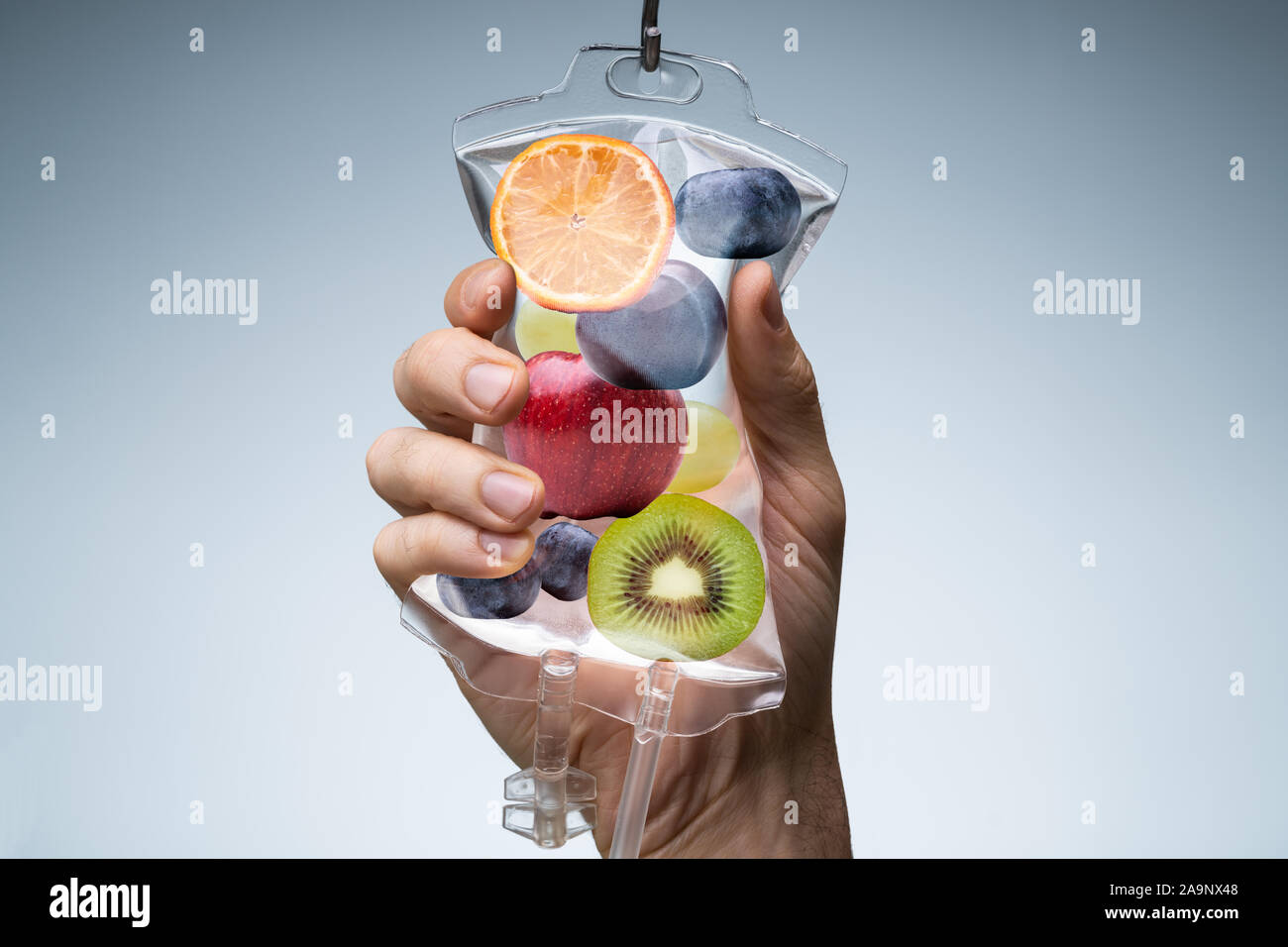 Person's Hand Holding sac rempli de solution saline différentes tranches de fruits contre fond gris Banque D'Images