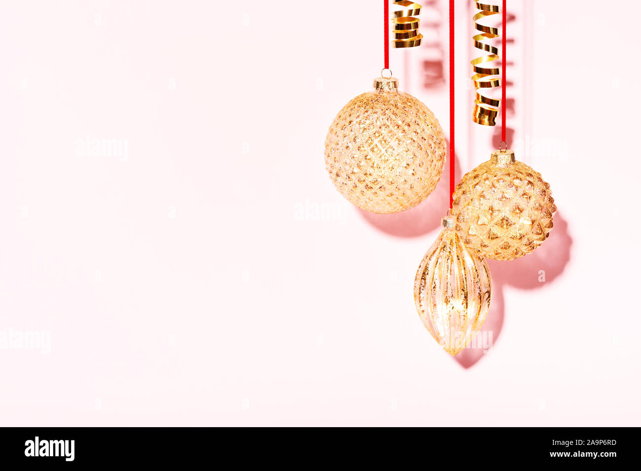 Trois golden Christmas baubles hanging contre le fond rose. Nouvelle Année style minimal concept. Banque D'Images