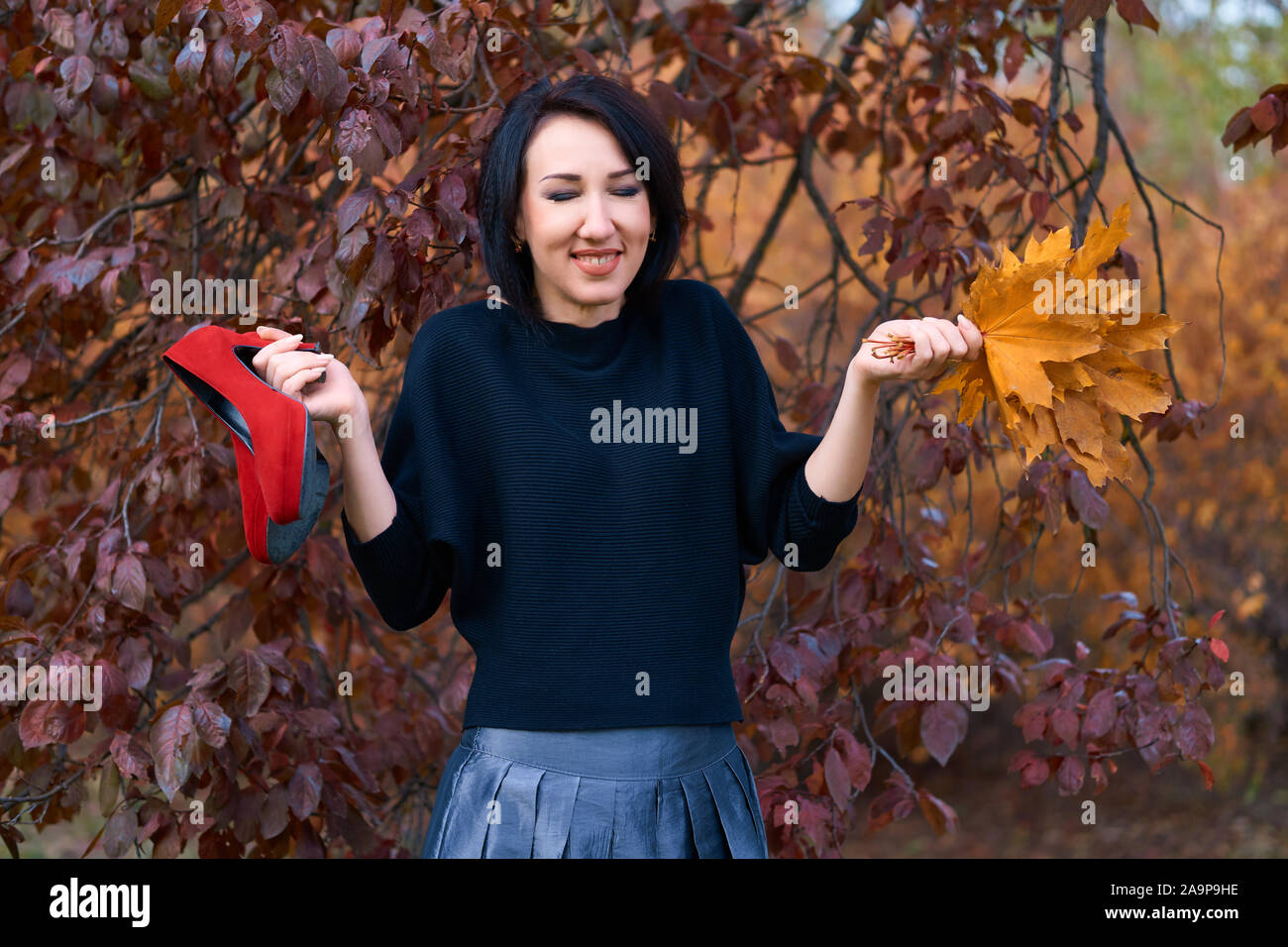 Belle femme élégante s'amusant et posant avec un bouquet de feuilles jaunes et rouges en automne chaussures city park Banque D'Images