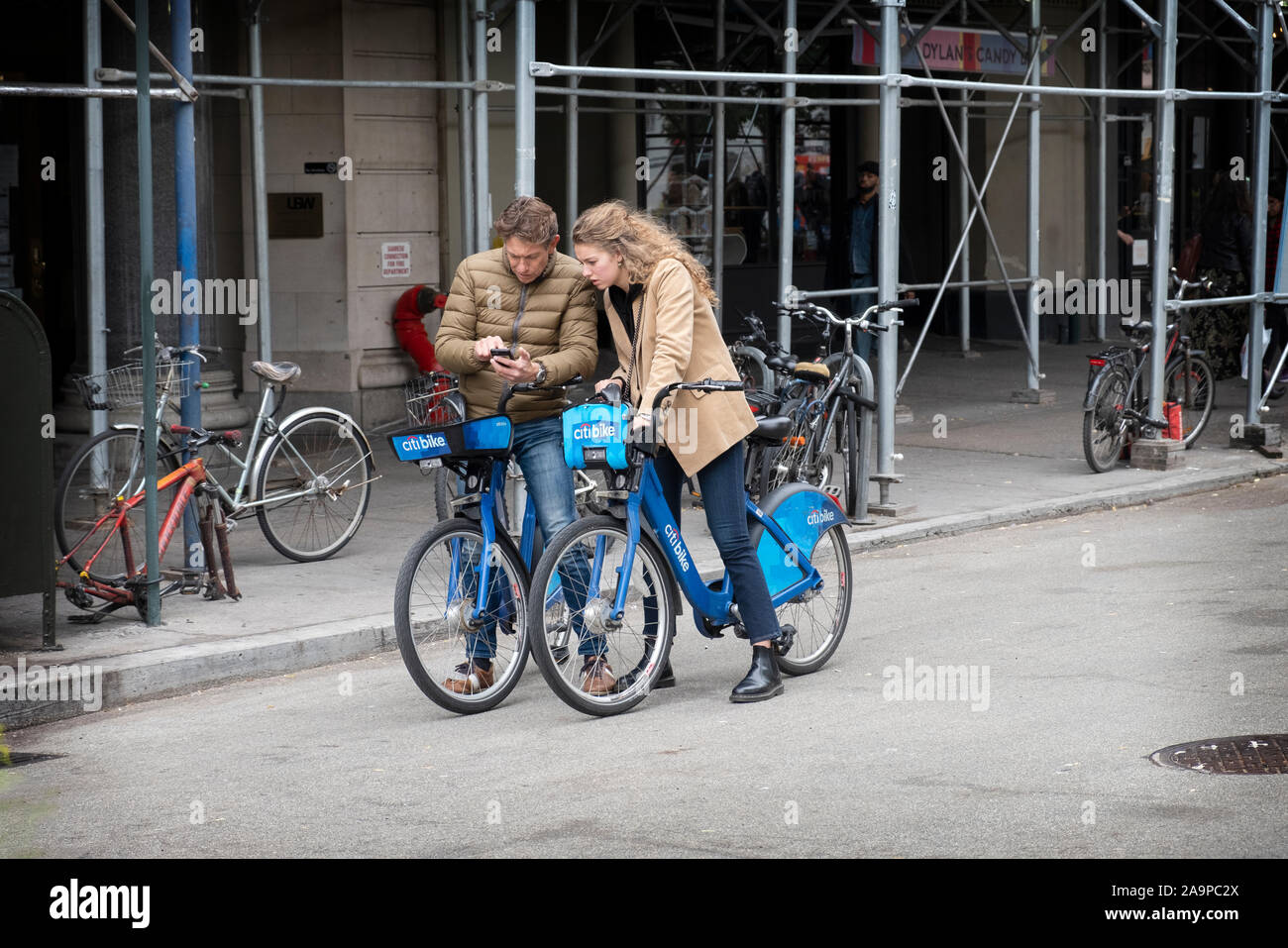 Un couple bien habillé, peut-être les touristes, s'asseoir sur leurs vélos de Citi en regardant un téléphone cellulaire. On Union Square West dans Lower Manhattan, New York Cit. Banque D'Images