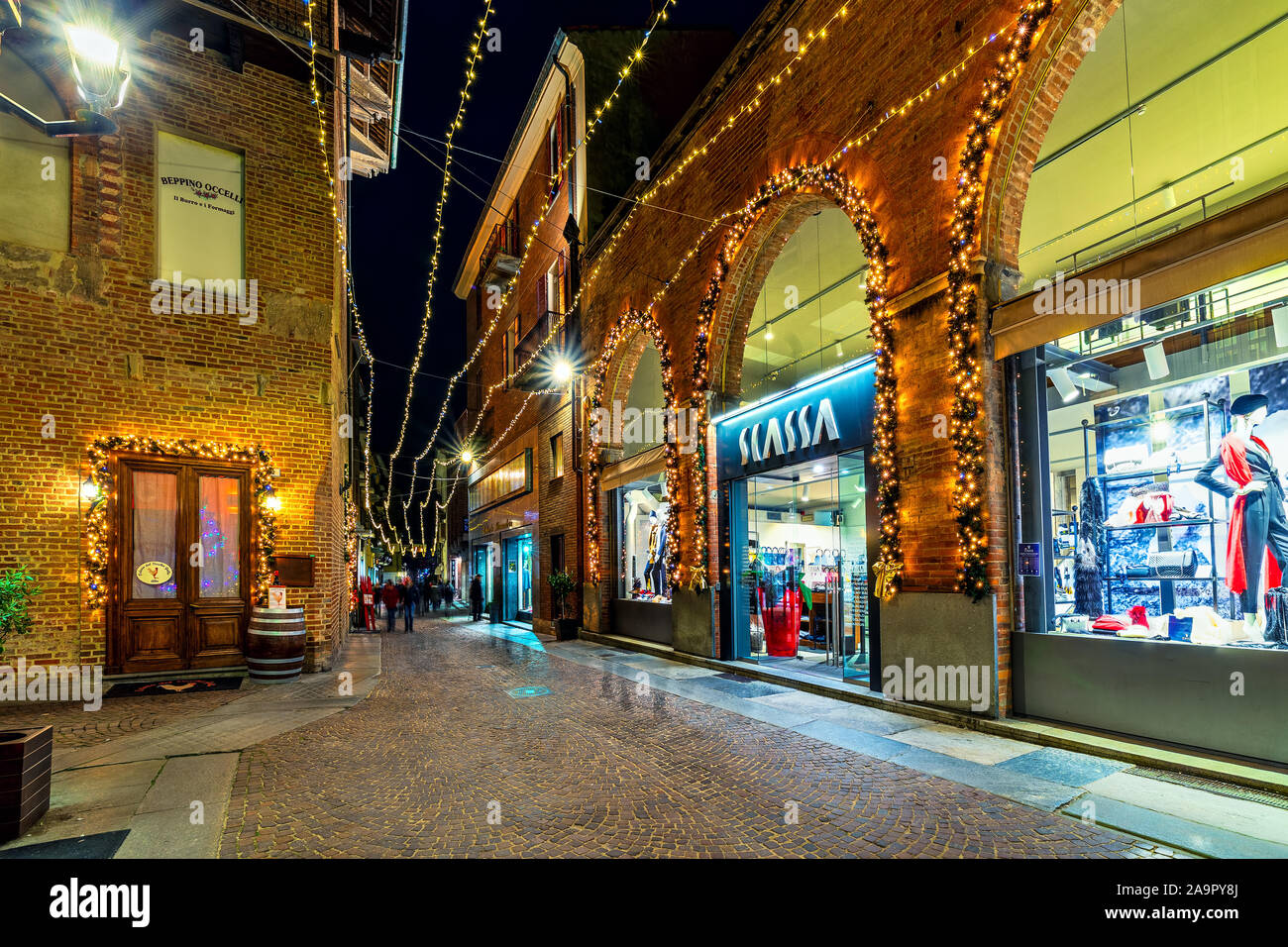 Rue piétonne pavée et de boutiques décorées avec illumination de Noël à Alba, Piémont, Italie du Nord. Banque D'Images